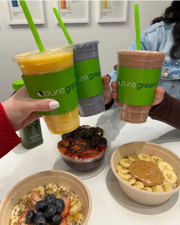 Hands toasting Pure Green smoothies over acai bowls at the Carlsbad juice bar