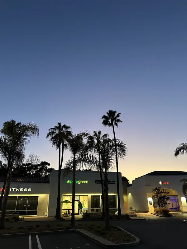 Pure Green Carlsbad storefront lit up at dusk with palm trees