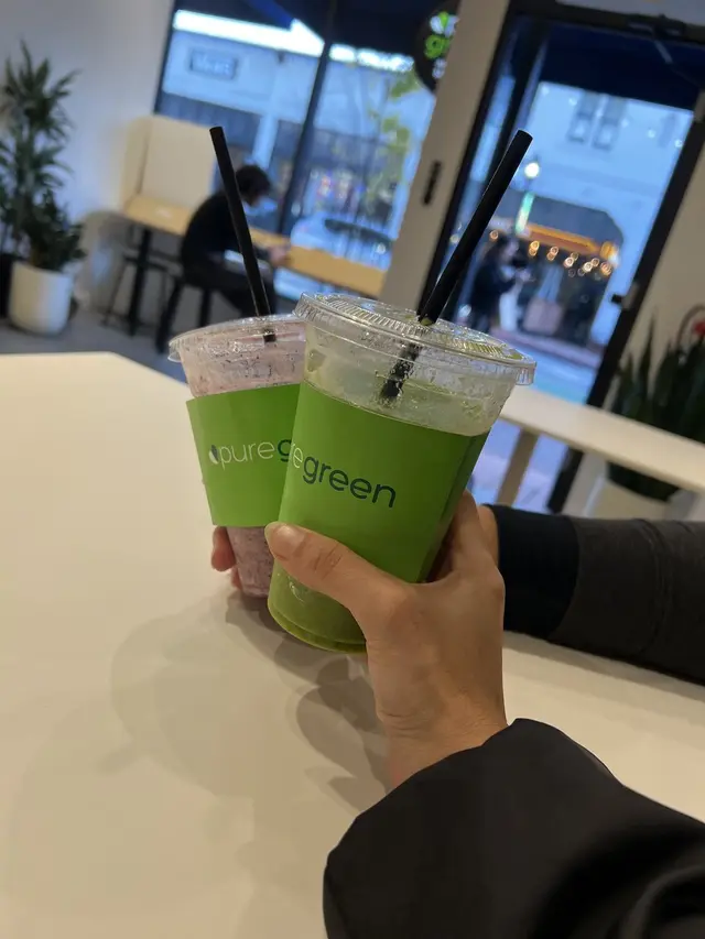 Guest holding a green smoothie by the window inside Pure Green SLO