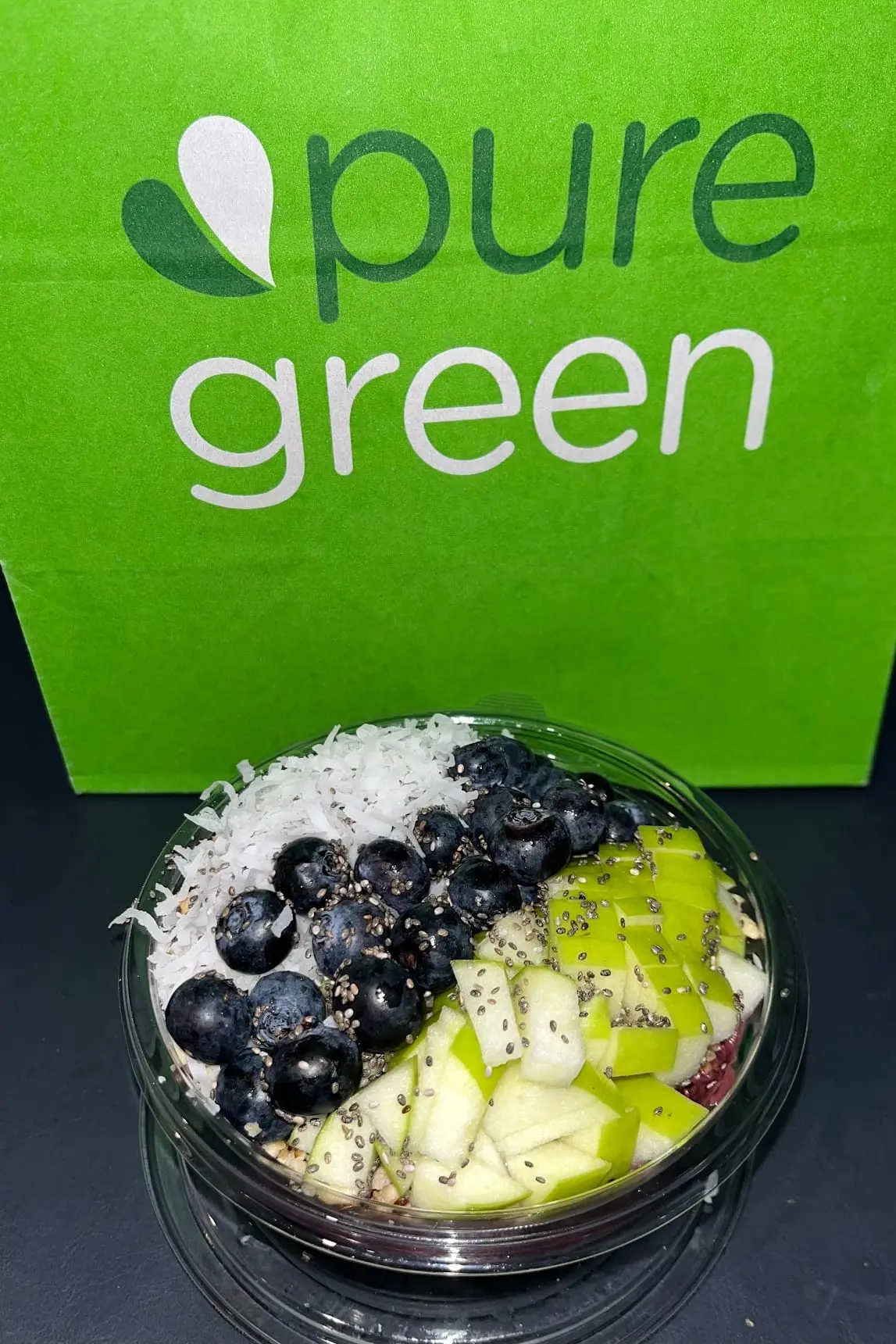 An acai bowl topped with blueberries, green apple, coconut and chia in front of a Pure Green bag at the Bed-Stuy store