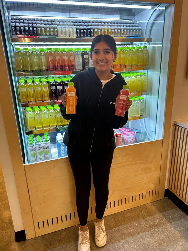 A team member with two cold-pressed juices at the fridge in Pure Green Fishers