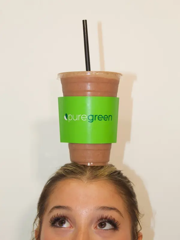 A Pure Green Madison smoothie balanced playfully on a customer's head