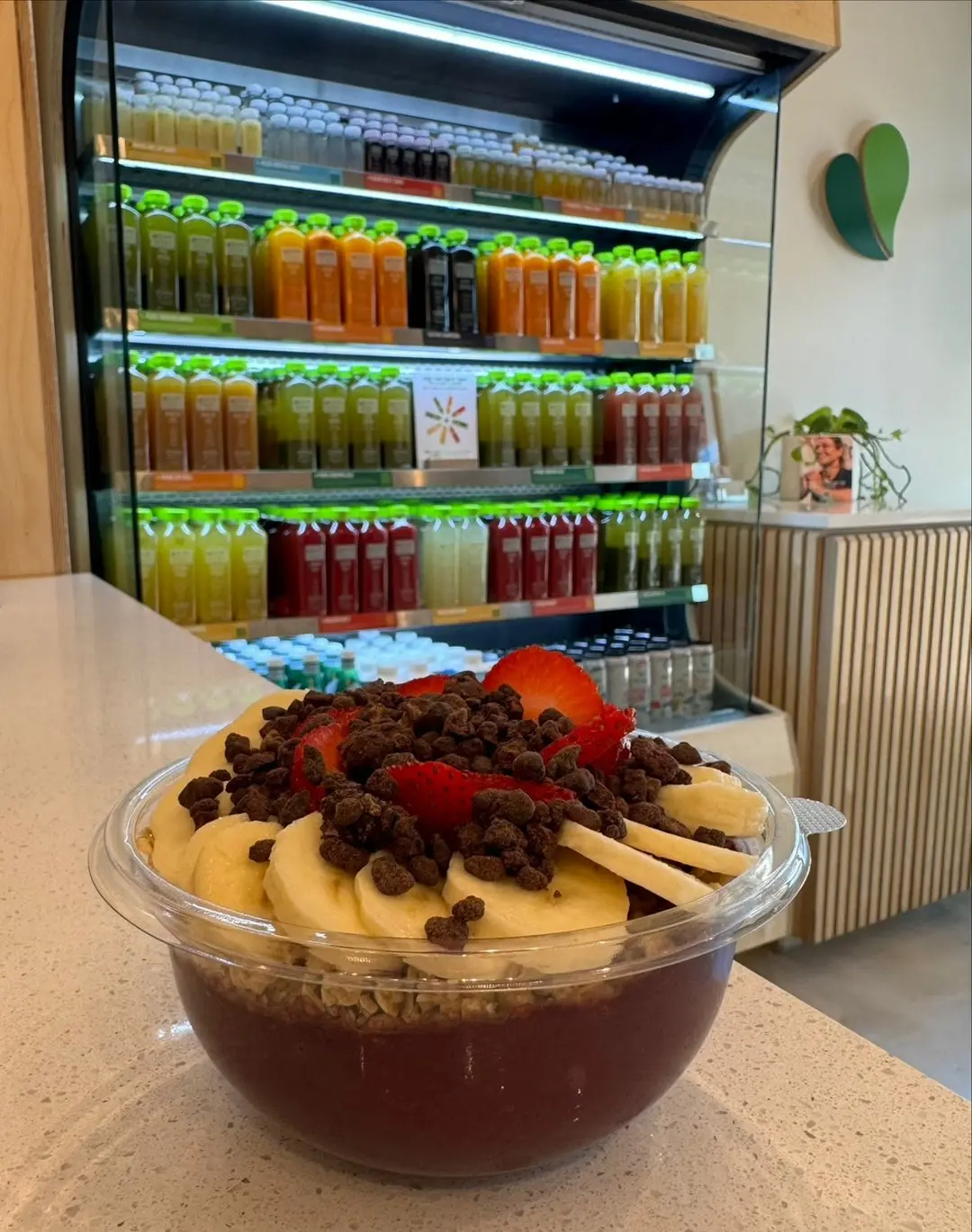 Acai bowl topped with granola and strawberries in front of the cold-pressed juice fridge at Pure Green Aventura