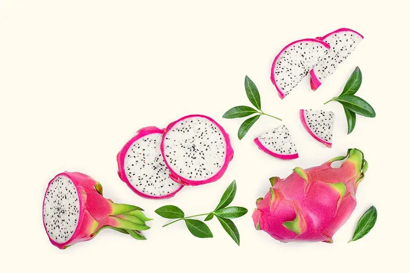 Fresh dragon fruit with bright pink skin, speckled flesh and green leaves