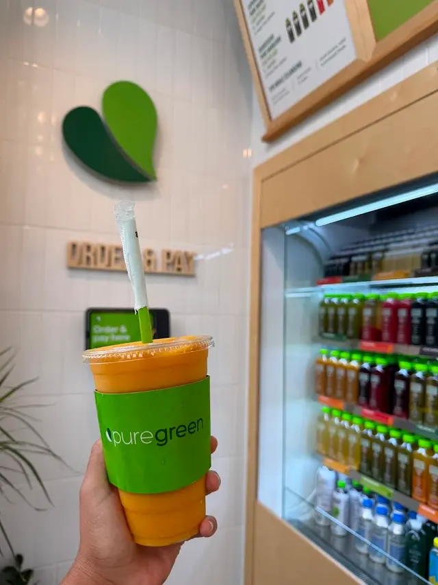 A mango smoothie held beside the cold-pressed juice fridge at Pure Green Tysons