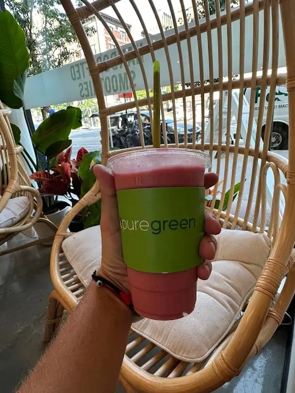 A Pure Green smoothie held up beside the hanging chair in Washington Heights