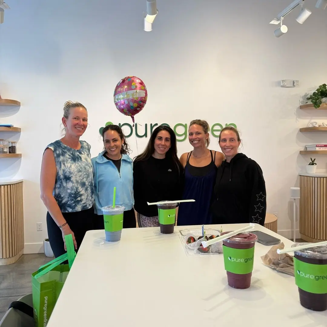 Guests gathered with Pure Green smoothies by the wall logo inside the Coral Springs store