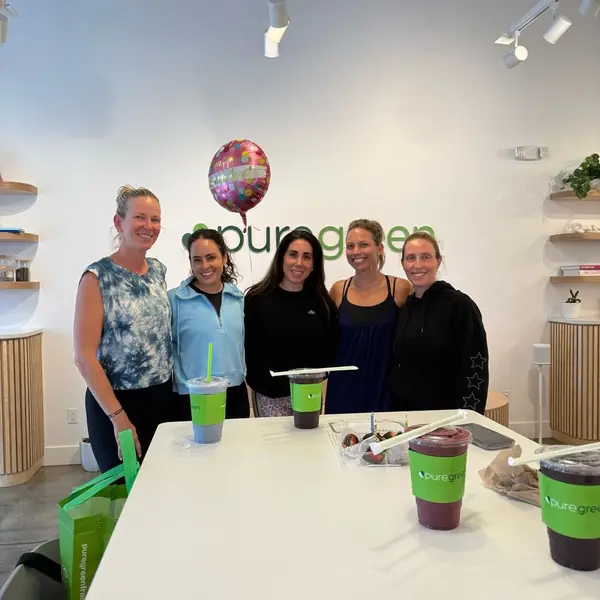Guests gathered with Pure Green smoothies by the wall logo inside the Coral Springs store