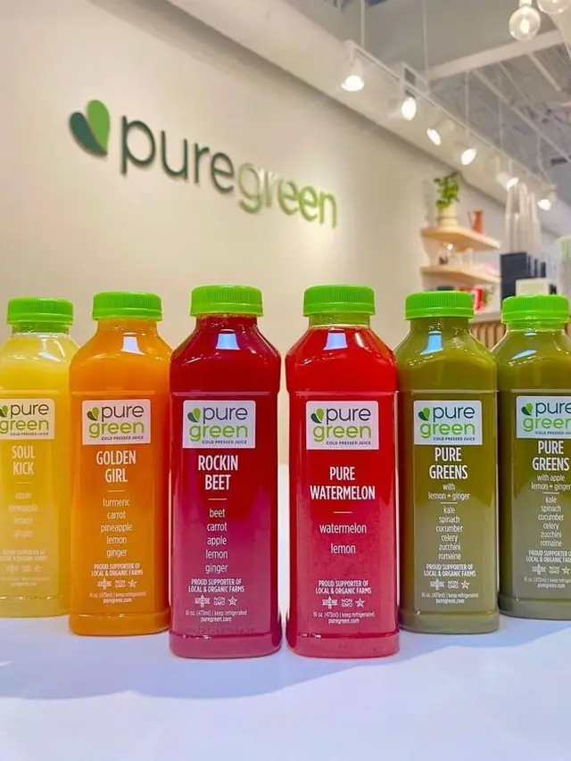 Six bottles of Pure Green cold-pressed juice lined up beneath the wall logo in Bethesda