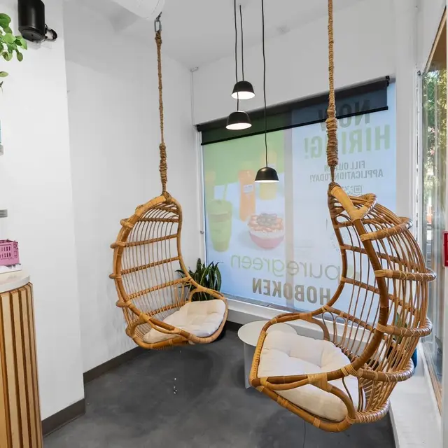 Two hanging rattan chairs by the window inside Pure Green Hoboken