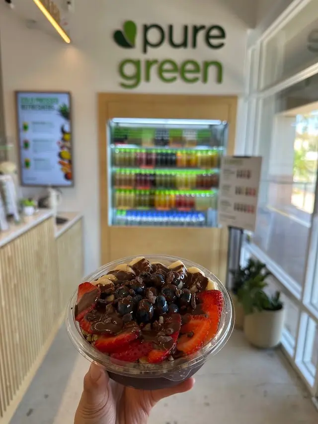 An acai bowl with strawberries, blueberries and chocolate drizzle held in front of the cold-pressed juice fridge