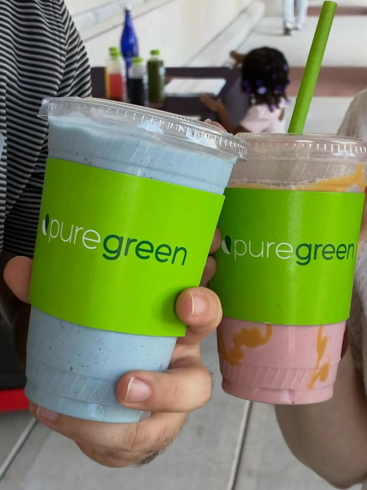 Two Pure Green smoothies in branded cups held up at the Boynton Beach store