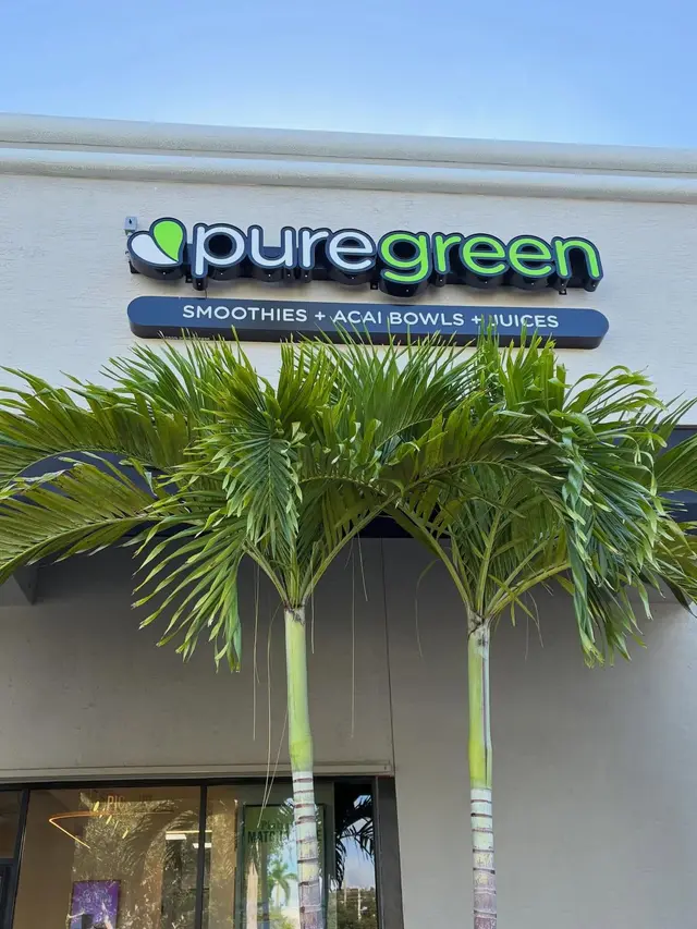 The Pure Green Boynton Beach shopfront sign framed by palm trees
