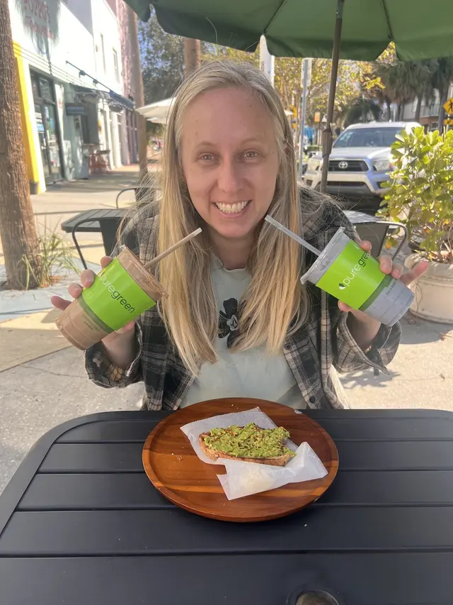 A guest with two cold-pressed juices and avocado toast on the patio at Pure Green St. Pete
