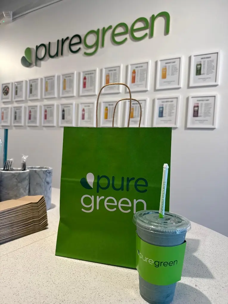 A green Pure Green bag and a smoothie on the counter beneath the wall logo and juice menu at Pure Green Wilkes-Barre