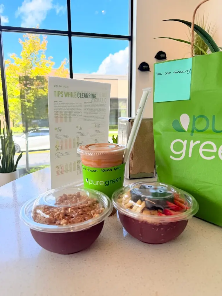 Two acai bowls, a smoothie and a green Pure Green bag on a table by the window at Pure Green Westerville