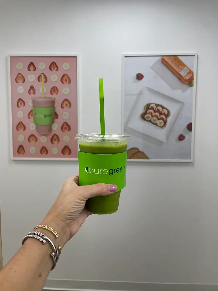 A green smoothie held up beside the framed prints at Pure Green The Woodlands