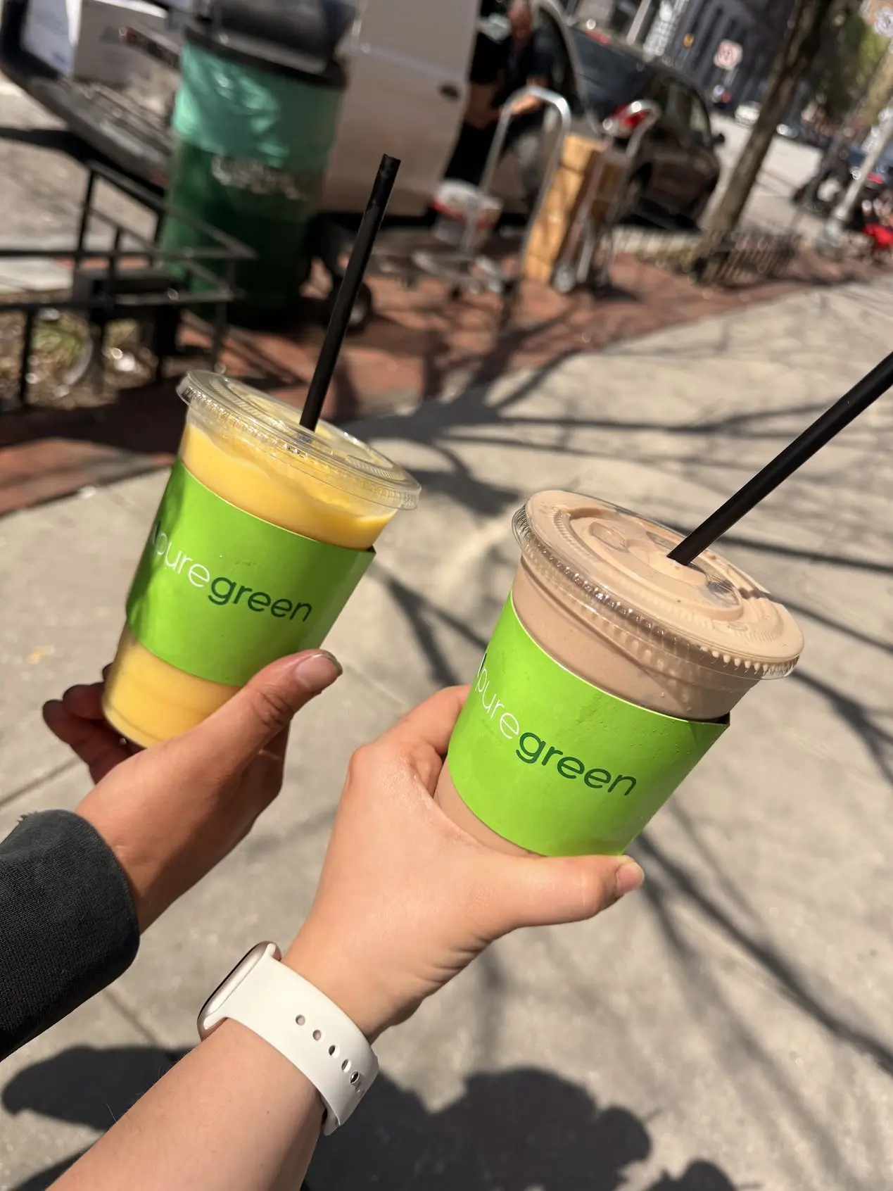 A mango smoothie and a mocha cold brew held up outside Pure Green Charles Village