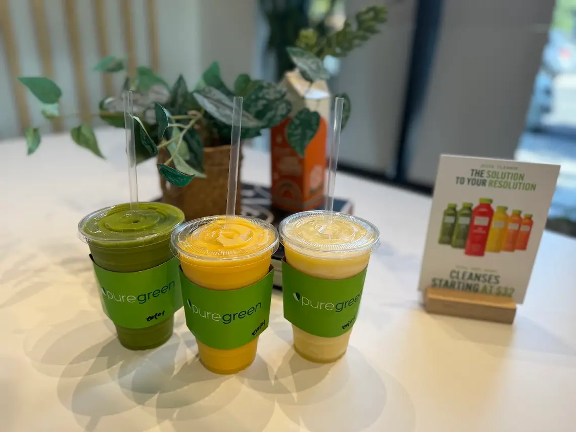 Three smoothies on the table beside the juice cleanse card at Pure Green Greenpoint