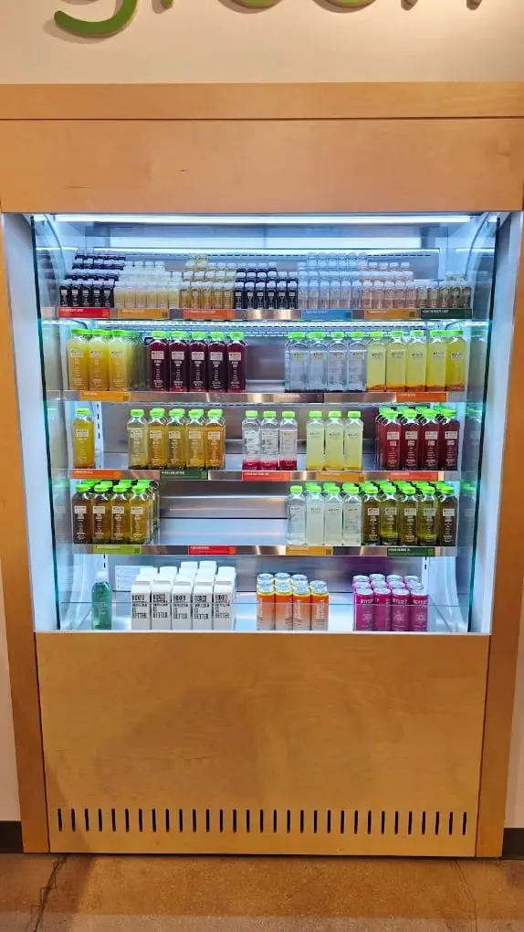 The cold-pressed juice fridge under the wall logo at Pure Green Logan Square