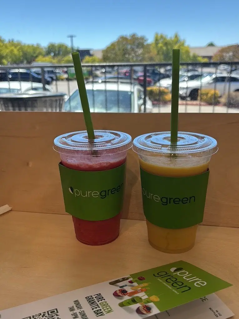 Two Pure Green smoothies with green straws on a wooden ledge outside the store