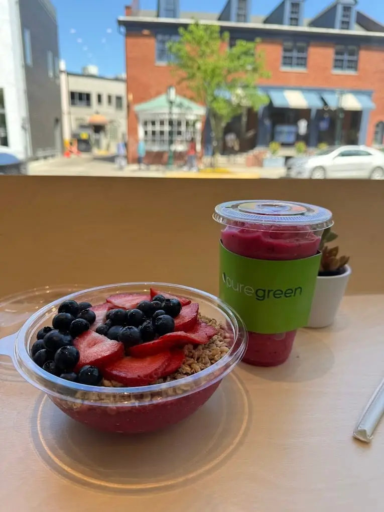 An acai bowl topped with berries and a drink by the window at Pure Green Birmingham