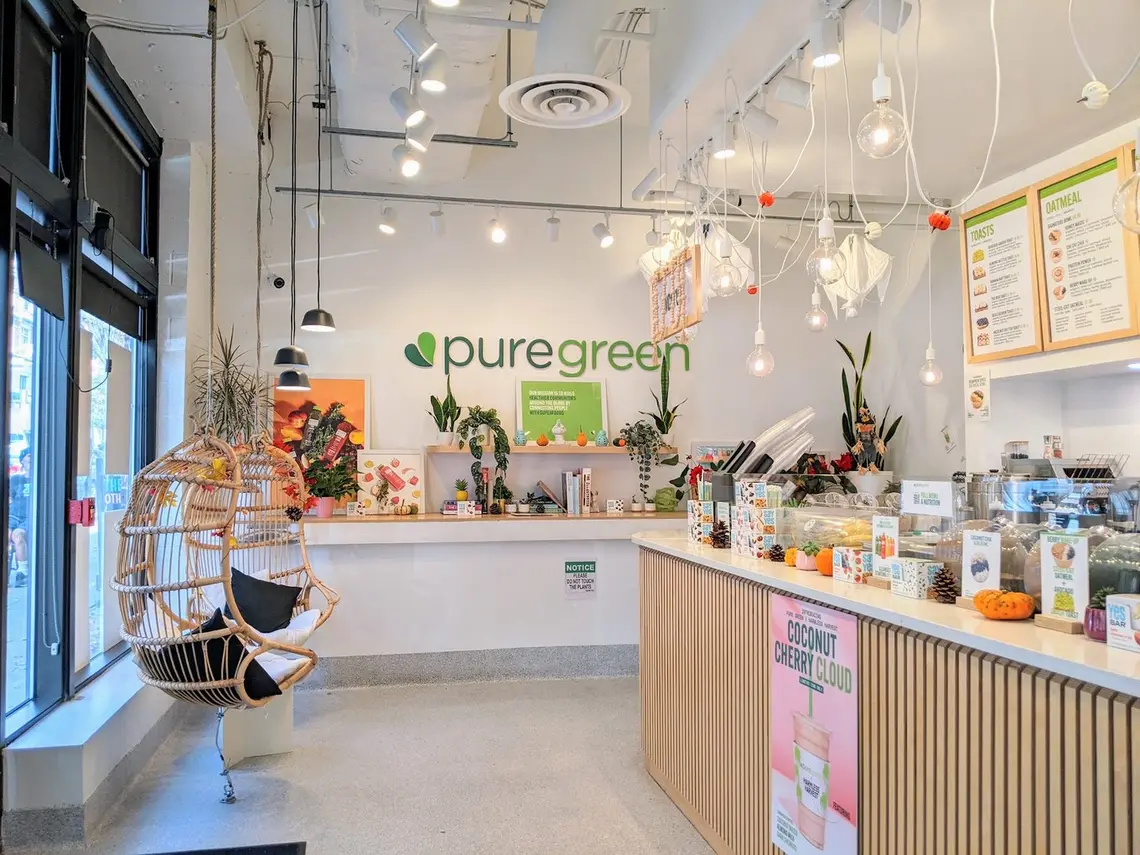 The order counter, hanging chair and logo wall inside Pure Green Charles Village