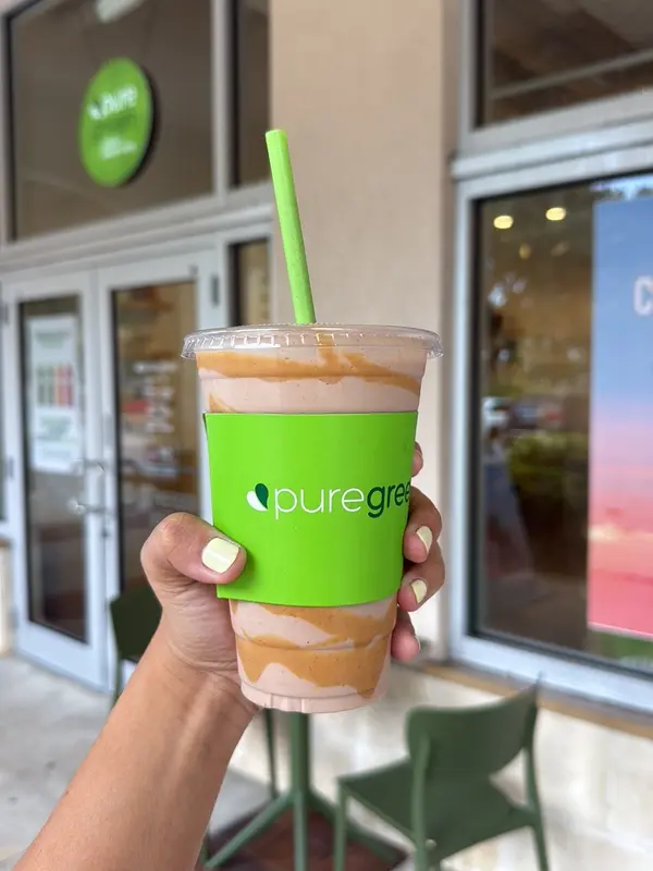 Guest holding a Pure Green smoothie in front of the Coral Springs storefront