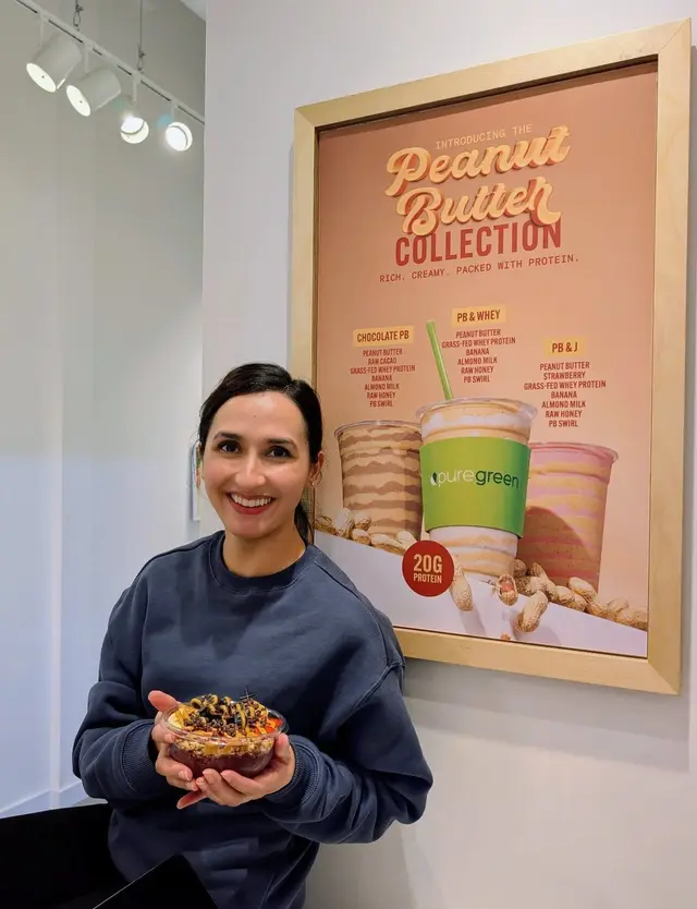 Guest holding an acai bowl by the Peanut Butter Collection display at Pure Green SLO