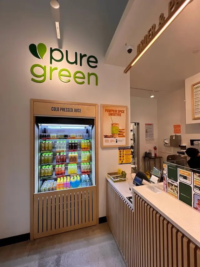The cold-pressed juice fridge beneath the wall logo at Pure Green Park Slope