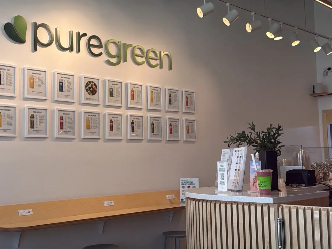 The Pure Green wall logo above framed juice cards beside the counter in Frisco