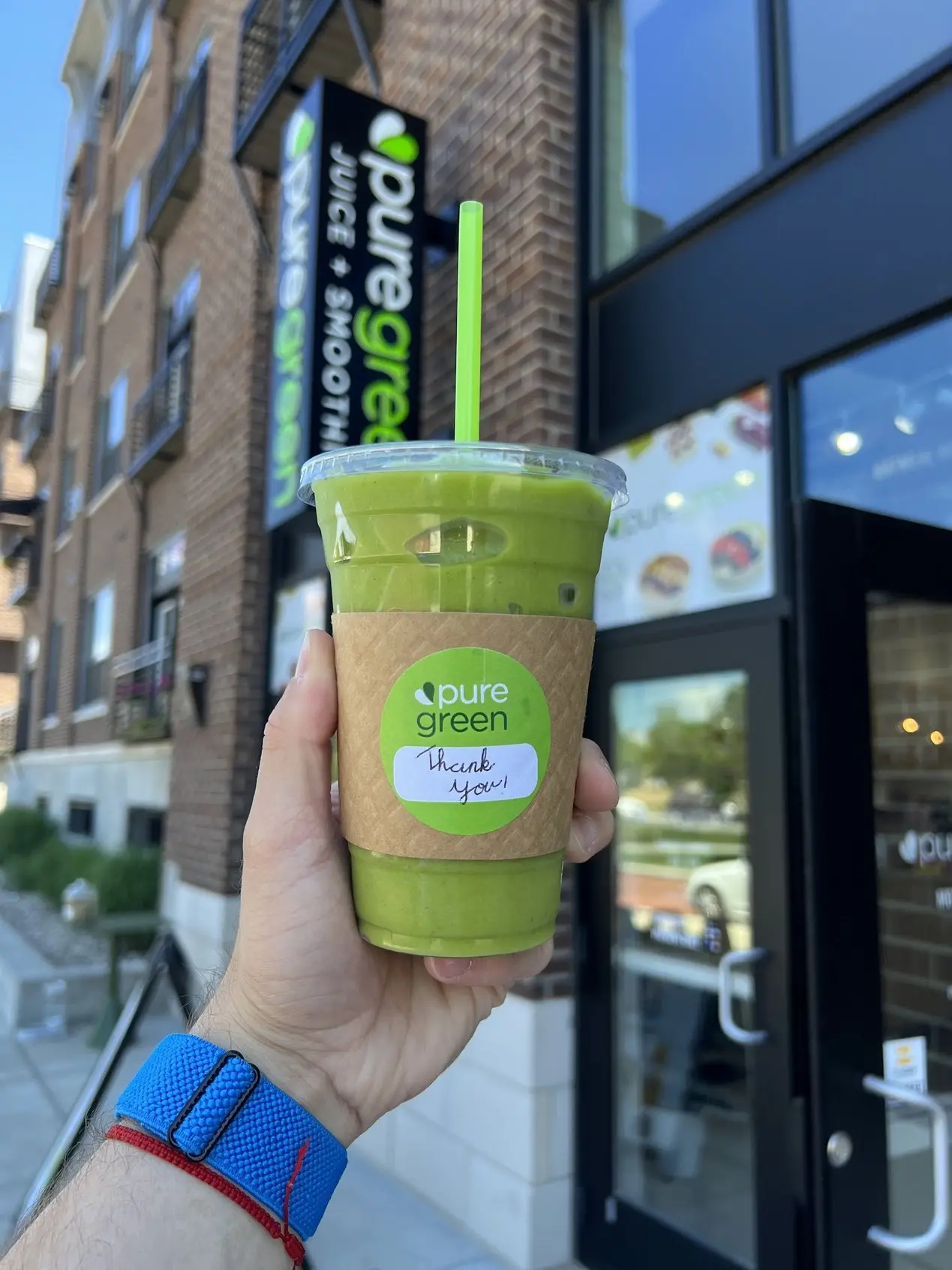 A green smoothie held up outside Pure Green Midtown Carmel