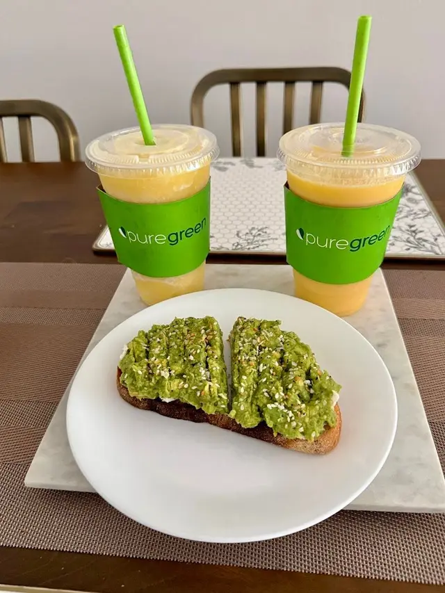 Two Pure Green smoothies beside an avocado smash toast on a marble board