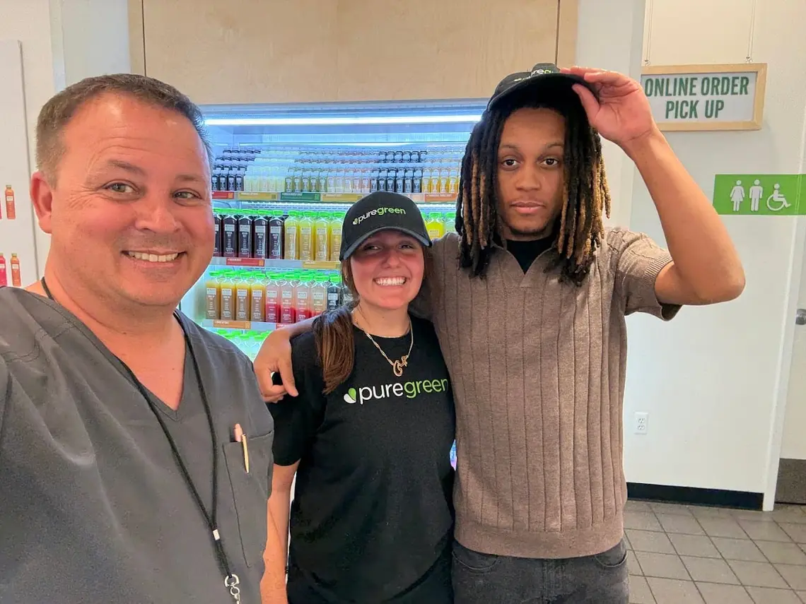 Two Pure Green Birmingham team members with a guest at the cold-pressed juice fridge