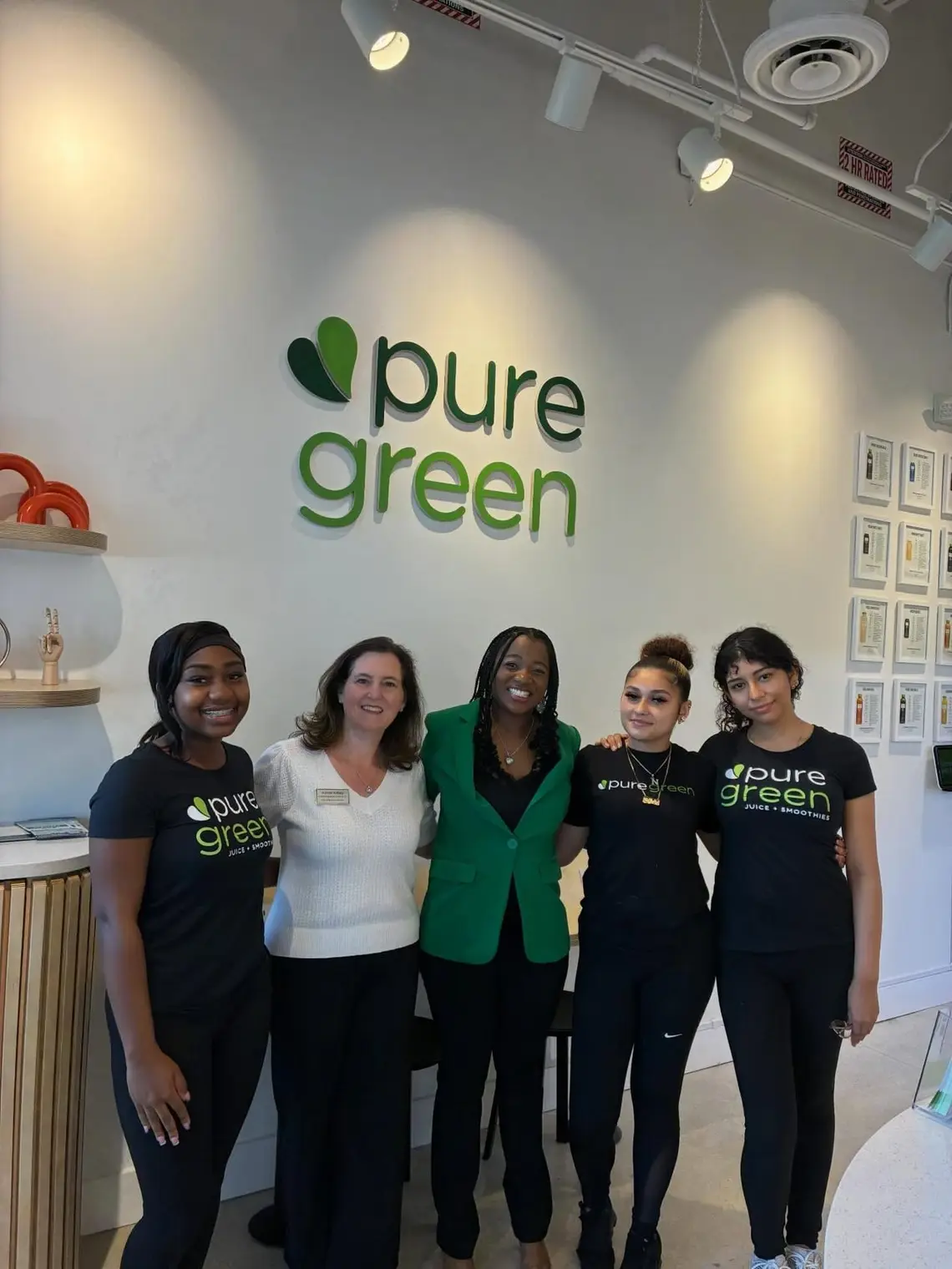 Five Pure Green Boynton Beach team members together beneath the store’s wall logo
