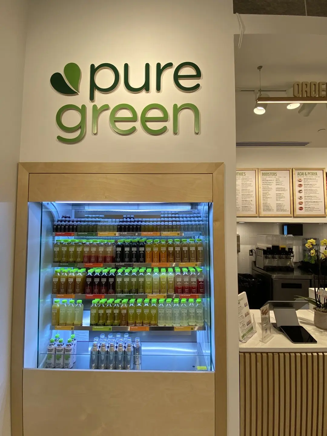 Cold-pressed juice fridge beneath the pure green wall logo at the SLO store