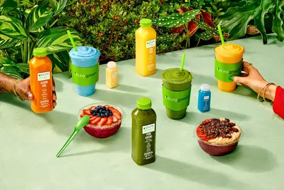 Pure Green cold-pressed juices, smoothies and açaí bowls arranged on a green table