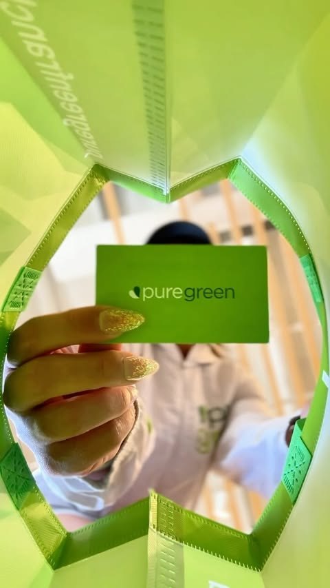 Hand holding a Pure Green gift card with a branded Pure Green bag