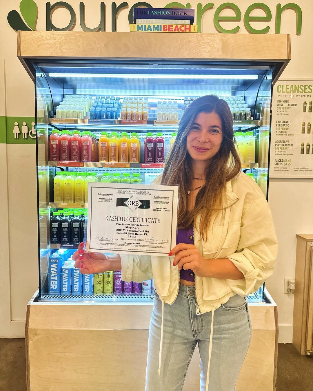 Pure Green Garden Shops team member with a certificate by the juice fridge