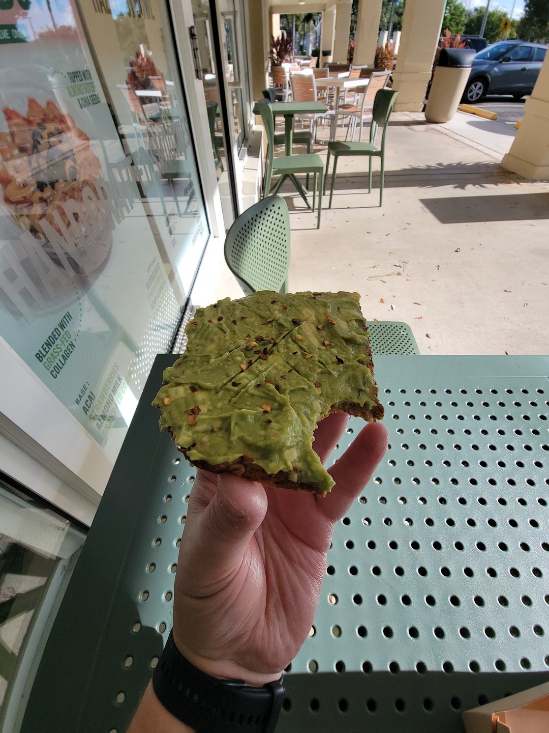 Hand holding a Pure Green avocado toast by the outdoor seating at the Garden Shops store