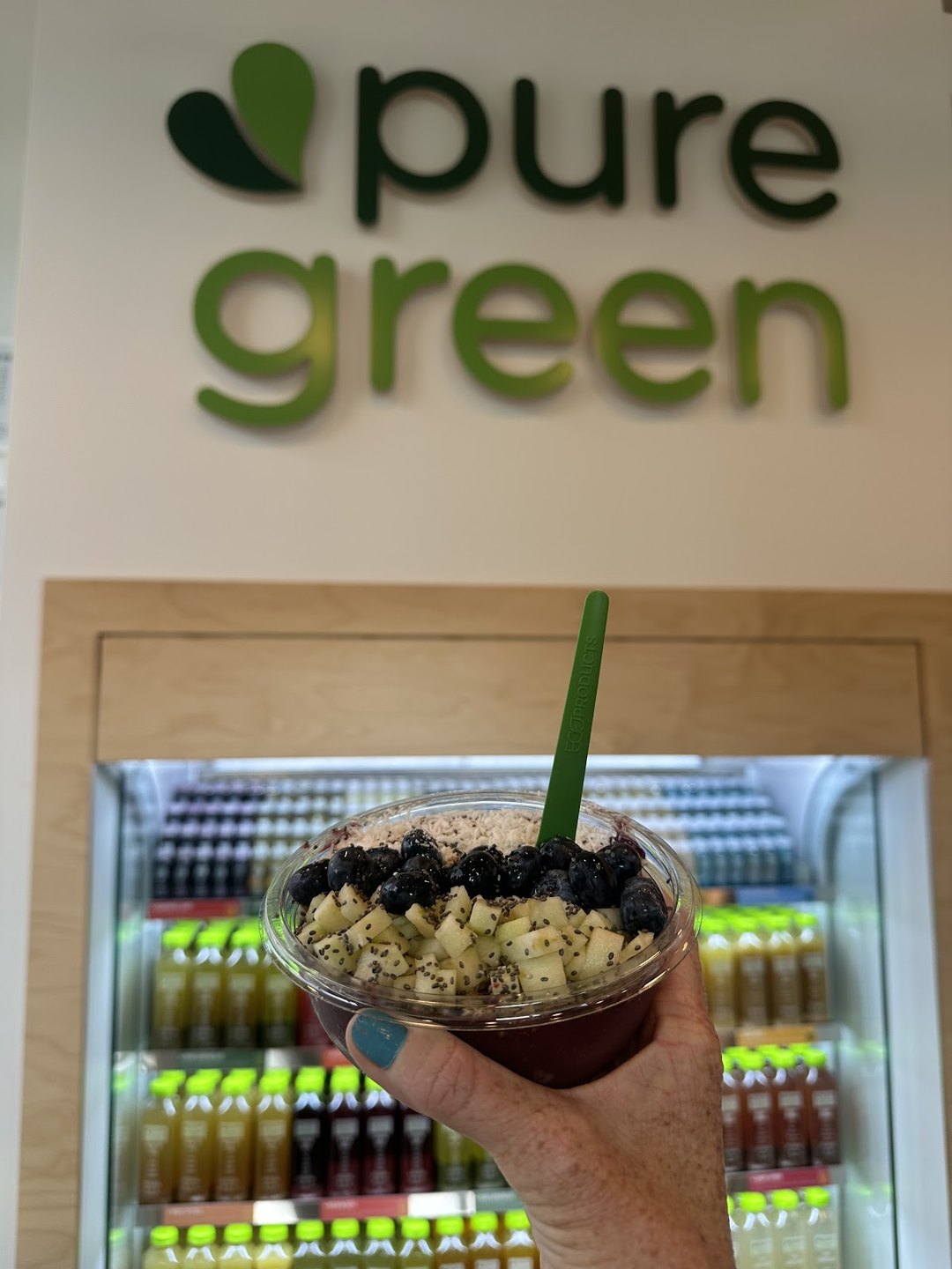 Guest holding an acai bowl in front of the cold-pressed juice fridge at Pure Green Fort Collins