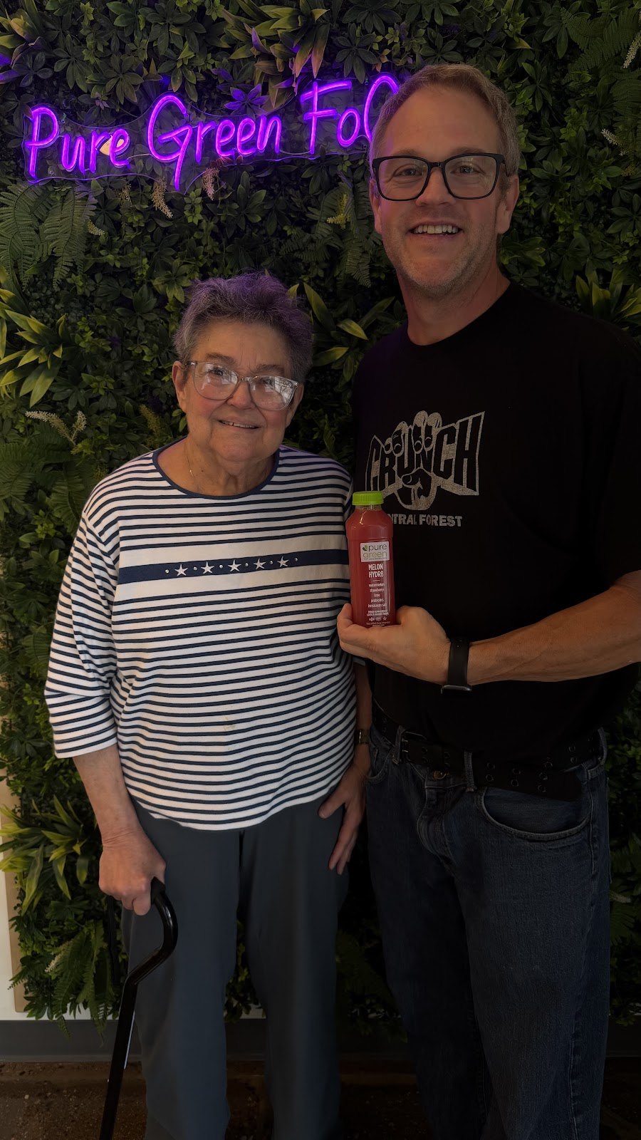 Guests holding a Rockin Beet cold-pressed juice by the Pure Green FoCo neon sign