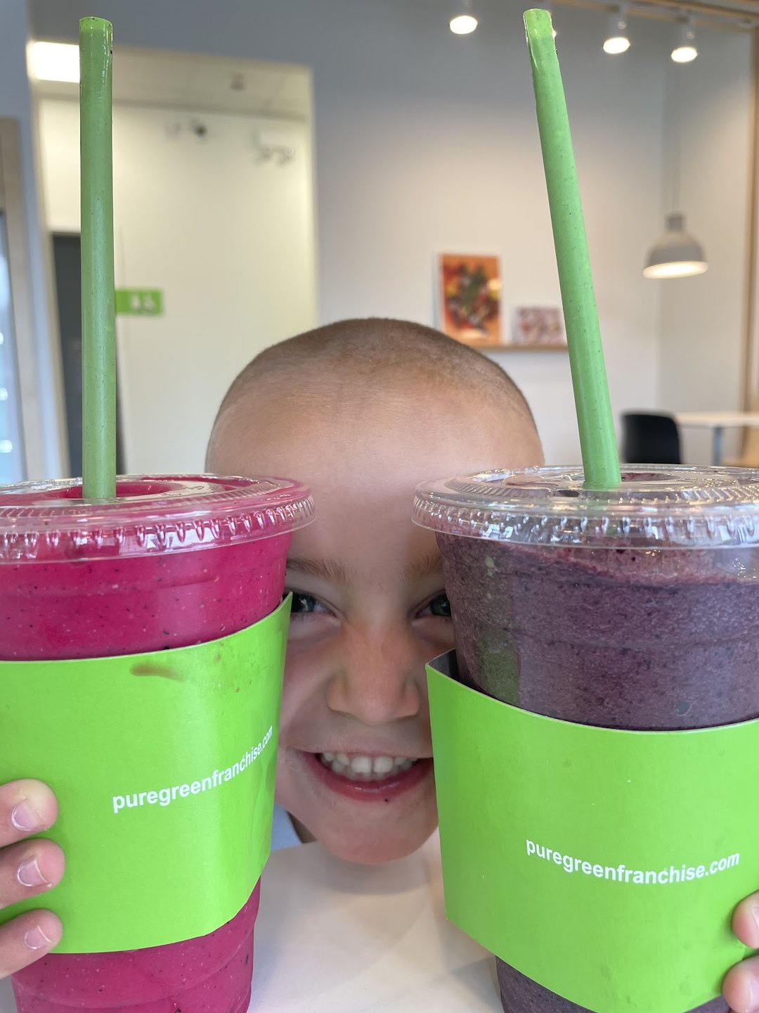 Child peeking between two Pure Green smoothies at the Fort Collins store
