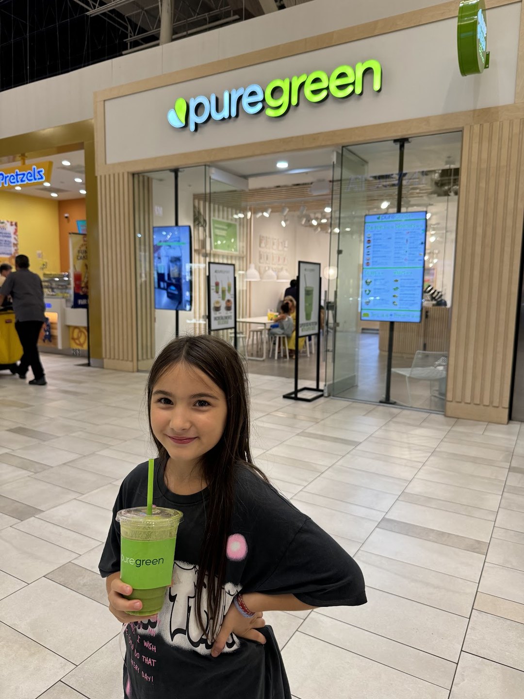 Young guest holding a green smoothie in front of the Pure Green Sawgrass Mills kiosk