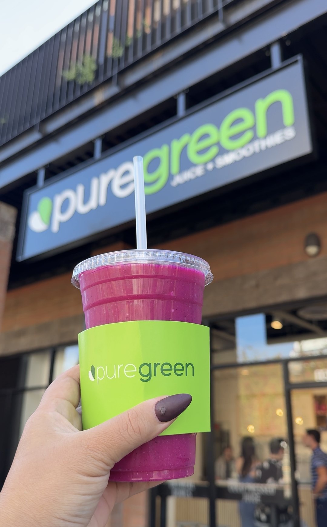 Guest holding a pink Pure Green smoothie in front of the Tempe storefront sign