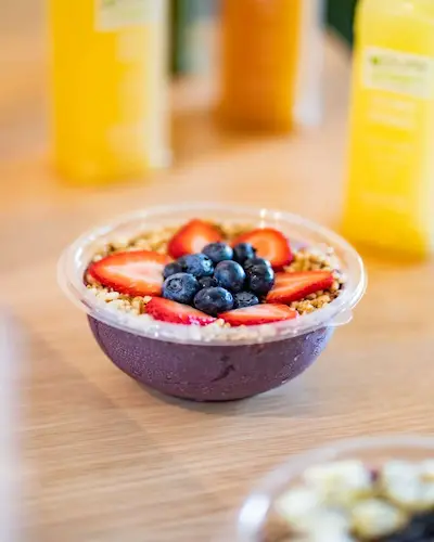 Acai bowl topped with strawberries and blueberries with juice bottles in the background at Pure Green Fulton Market