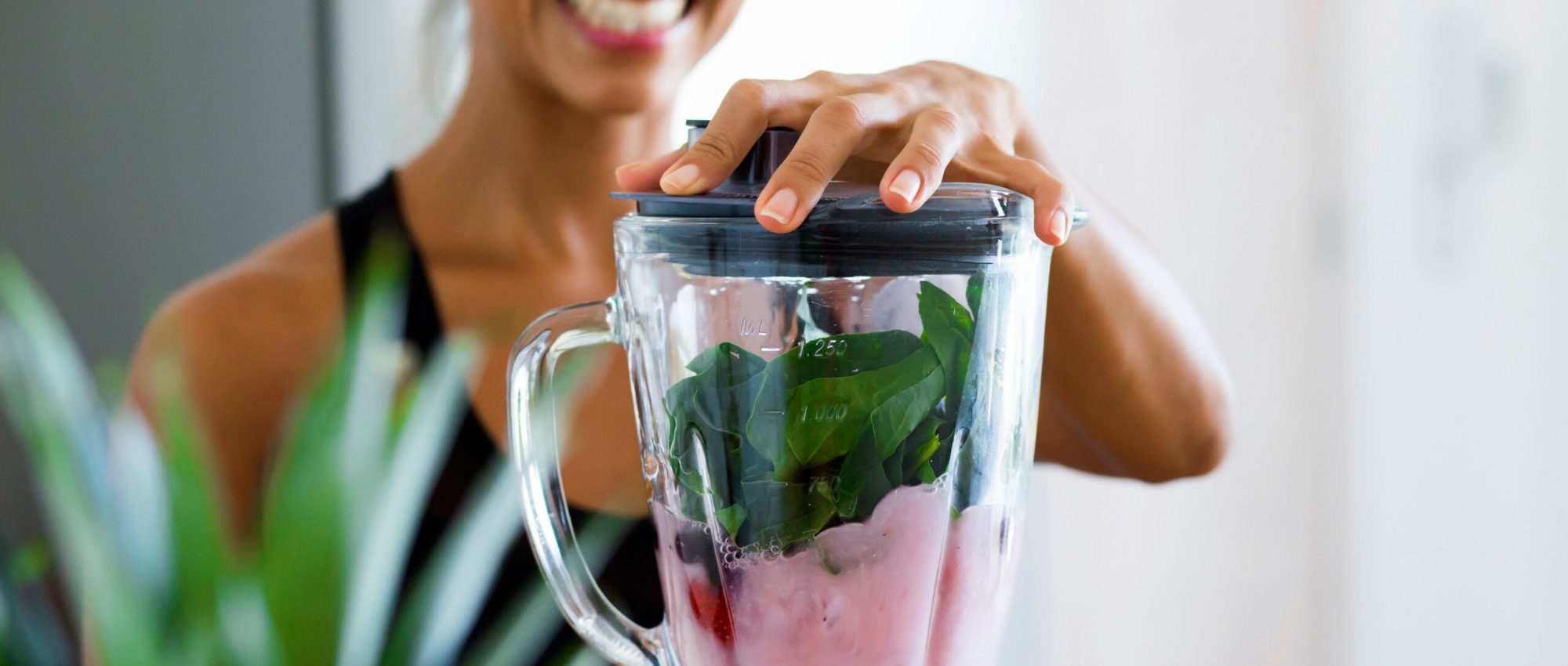 Woman blending spinach, berries, bananas and almond milk to make a healthy green smoothie